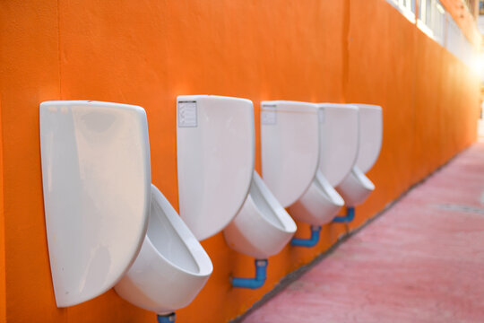 Row of Public urinals hanging on an orange wall
