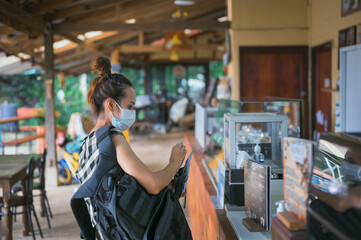 Side view point of young women wearing surgical mask with backpack buying coffee at coffee shop in small village , chiang mai north of thailand , travel concept