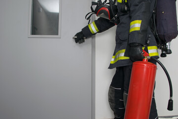 firefighter in protective clothing and with a fire extinguisher, opens the iron door, there is a...