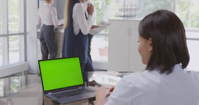 View over shoulder of african businesswoman sitting at desk looking at laptop green screen
