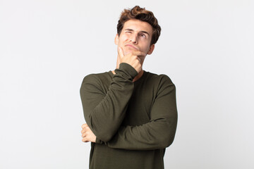 young handsome man thinking, feeling doubtful and confused, with different options, wondering which...