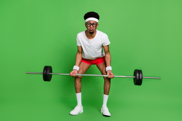 Photo of funny nerd bodybuilder guy lift heavy barbell grimace wear white t-shirt isolated green...