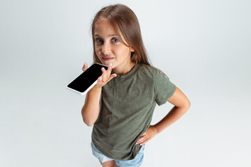 Naklejka premium Close-up portrait of beautiful preschool smiling girl with phone isolated on white studio background. Copyspace for ad. Childhood, education, emotion concept