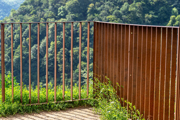 Rusty metal fence at the edge of the river valley, visible trees on the hills.