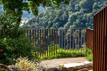 Rusty metal fence at the edge of the river valley, visible trees on the hills and river.