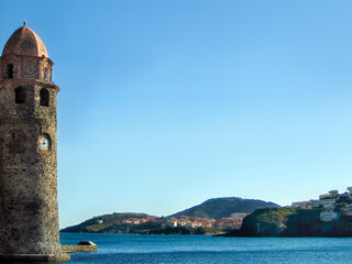 A city on coast of the sea surrounded by mountains with high old brick tower and plane in blue sky. Travel in east.