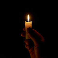 A hand holding a lighted candle in the dark. The light of a burning candle in a dark room. A candle...
