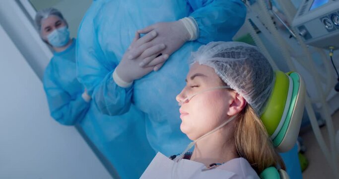 A close-up female patient in a disposable hat is going down to a lay position in a dental chair, she is under anesthesia.