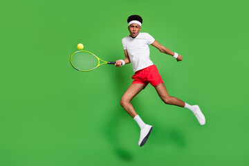 Fototapeta na wymiar Full length photo of funky serious dark skin man wear white t-shirt jumping high playing squash isolated green color background