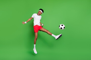 Fototapeta na wymiar Photo of energetic guy jump open mouth leg hit ball wear white t-shirt shorts footwear isolated green color background