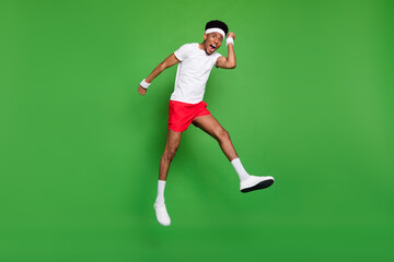 Plakat Full length photo of lucky funky dark skin guy dressed sport outfit jumping high rising fists isolated green color background