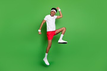 Full length body size view of attractive cheerful guy sportsman jumping having fun rejoicing isolated over bright green color background