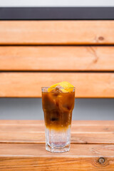 Espresso tonic with ice in a highball glass garnished with an orange zest, on a wooden backdrop