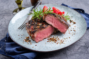 Modern style traditional barbecue entrecote beef steak with tomatoes und herbs served as close-up on a design plate