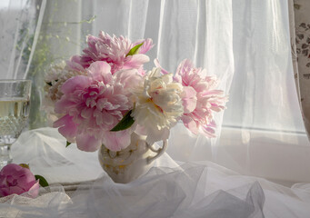 A bouquet of delicate peonies on the windowsill in the rays of the evening sun.
