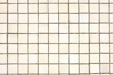 Background from a wall made of square beige mosaic tiles