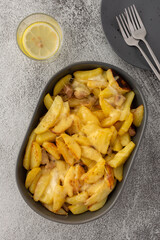 Stewed young potatoes with meat and cheese in an oval dish, lemon water in a glass, top view