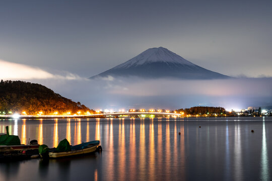 View of Mount Fuji covered with snow at sunset during a foggy day with boats along Lake Kawaguchi in foreground, Japan.