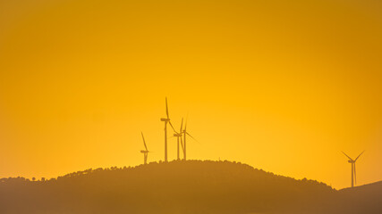 Landscape with wind turbines that produce electricity by rotating in the wind. Wind farm eco field. Eolic park with orange sky background.
