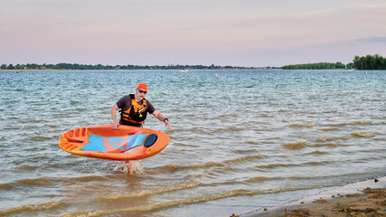 Senior male paddler is finishing his paddling with a prone kayak on Boyd Lake in Colorado