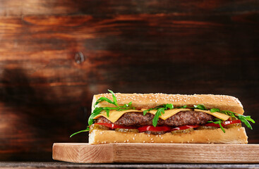 Grilled juicy baguette sandwich with cutlet and fresh vegetables on wooden background. Sandwich...