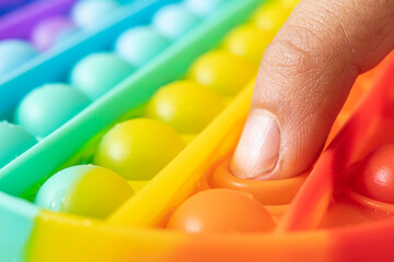 Macro of hands with Pop It sensory antistress. Kid play colorful rainbow pop it sensory toy, hands close-up. Concept of pop it sensory game for stressed child. - obrazy, fototapety, plakaty