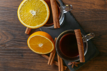 Mulled wine in glass cups with cinnamon and oranges on a wooden table.