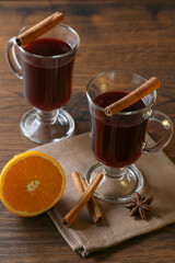 Mulled wine in glass cups with cinnamon and oranges on a wooden table.