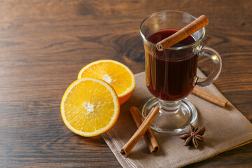 Mulled wine in glass cups with cinnamon and oranges on a wooden table.