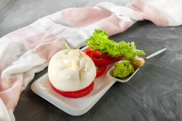 Fresh soft cream burrata cheese with tomatoes, green salad and pesto sauce on a beautiful white plate