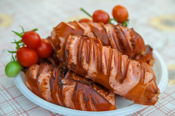 Sausages fried on an open fire. Grilled sausages with cherry tomatoes are on a disposable plate