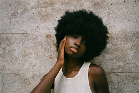 Confident young African American lady touching face and looking at camera