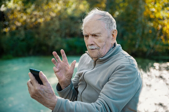 grey man takes a selfie from his mobile phone to post it on social media for communication. A man of 88 years old communicates with his grandchildren on a smartphone, active old age