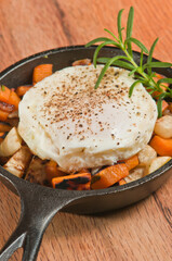 top view, close distance of a black cat iron pan , filled with roasted sweet potato and turnip hash with turkey and a poached egg with pepper and sprig of rosemary