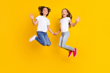 Full length body size view of two nice cheerful carefree kids jumping having fun good mood isolated over bright yellow color background