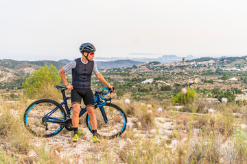 Fototapeta premium Professional cyclist with sportswear and helmet looking at the landscape on sunny day with his road bike