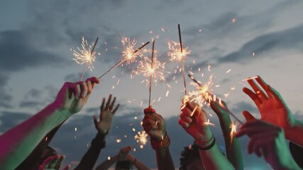 Handheld shot of unrecognizable young people holding sparklers and dancing on rooftop terrace on summer evening