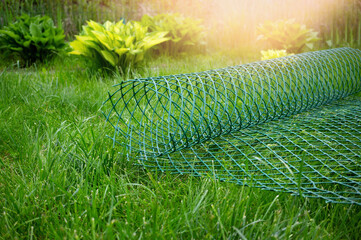 roll of plastic green mesh for the garden lies on the lawn. garden net for fixing plants and...