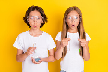 Portrait of two attractive amazed cheerful schoolkids making experiment isolated over bright yellow...