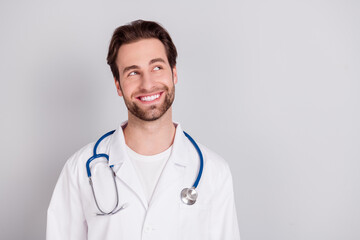 Photo of professional positive young doc man dressed white coat smiling looking empty space isolated grey color background