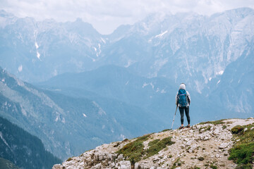 Woman trekker with backpack and trekking poles on the hill enjoying picturesque Dolomite Alps view near Tre Cime di Lavaredo formation in South Tyrol, Italy. Active people and mountain concept.
