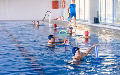 Company of people doing exercise with aqua noodles during water aerobics