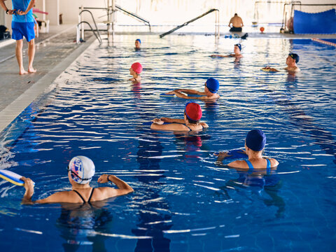 Company of people doing exercise with aqua noodles during water aerobics