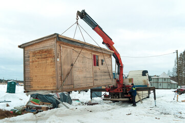 A truck with a crane manipulator loads a construction house on the construction site of a country house