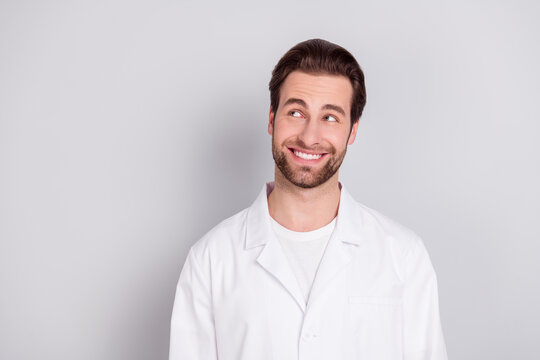 Photo of positive thoughtful young doc man dressed white coat smiling looking empty space isolated grey color background