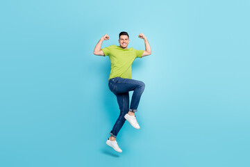 Fototapeta na wymiar Full length photo of positive young man jump up celebrate win raise fists isolated on blue color background