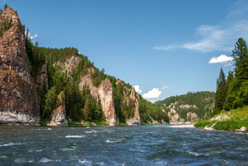 Landscape of Siberia. Kiya River, mountain banks and green forests in the Kemerovo region. Daytime landscape with blue skies and clouds.