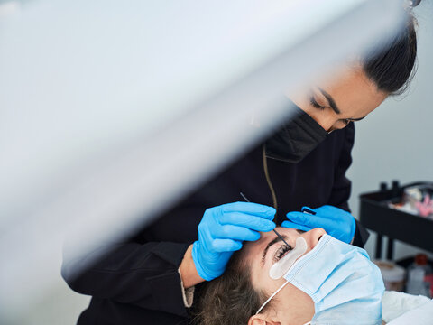 Beautician curling eyelashes of female client