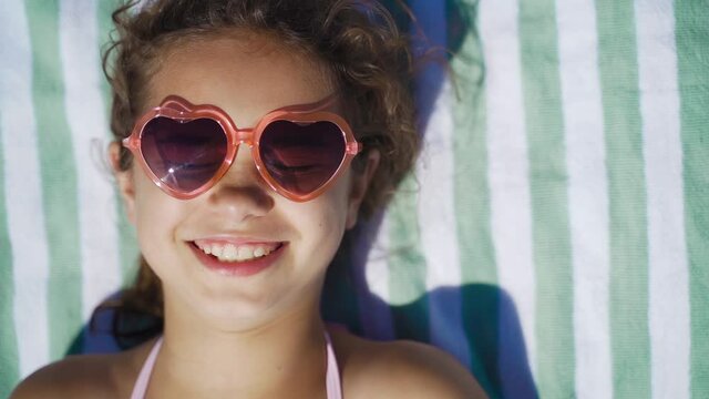 Cute girl in sunglasses sunbathing on the sea. Happy kid on the beach smiles and sunbathes. Portrait of a child on vacation, travel, tourism, vacation