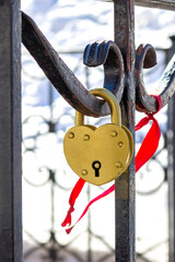 A heart-shaped lock on a wrought-iron fence next to a red ribbon. A symbol of a happy married life. Space for the text. Close up. Vertical layout.